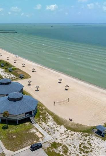 Aerial view of Rockport Beach Park with shade cabanas, a volleyball net, pavilions and calm Aransas Bay water